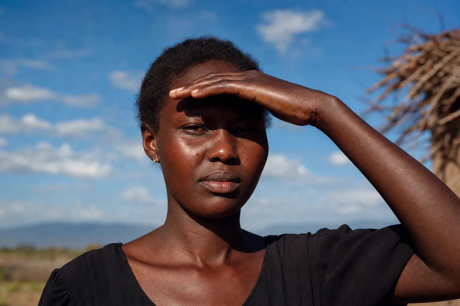 Black African woman shielding her glowing deep brown skin while standing in strong direct sunlight outdoors in Kenya