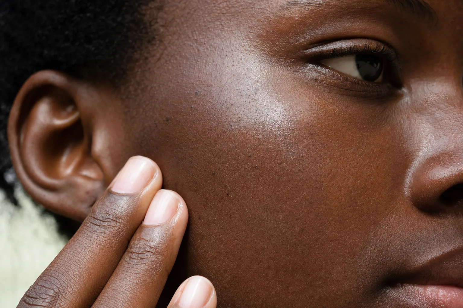 Close-up of sunscreen being massaged fully into the deep brown skin of a Black African woman's cheek with no white cast